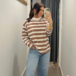 Woman taking a mirror selfie wearing a striped sweater and jeans in a hallway.
