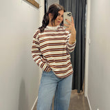 Woman taking a mirror selfie wearing a striped sweater and jeans in a hallway.