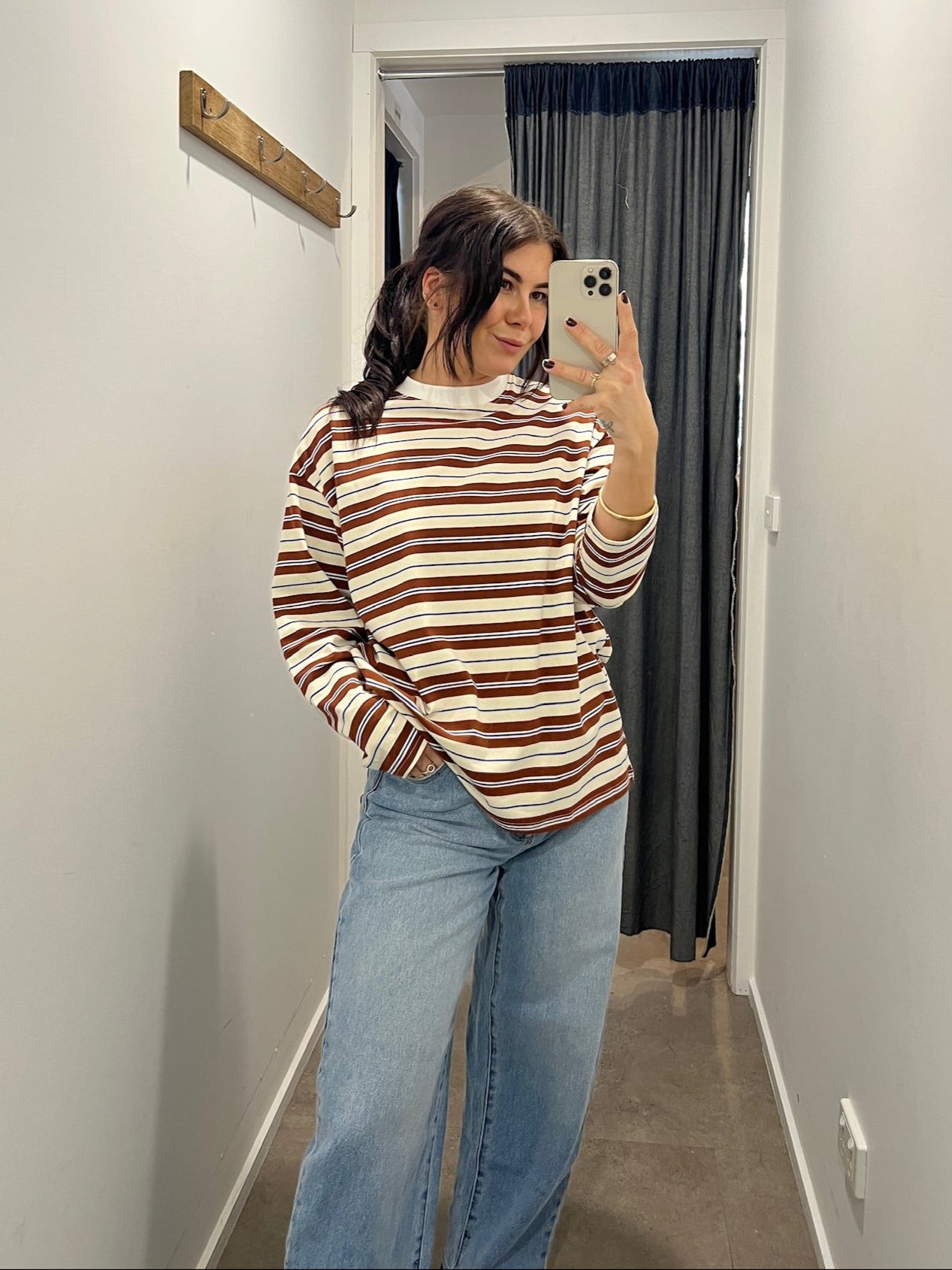 Woman taking a mirror selfie wearing a striped sweater and jeans in a hallway.