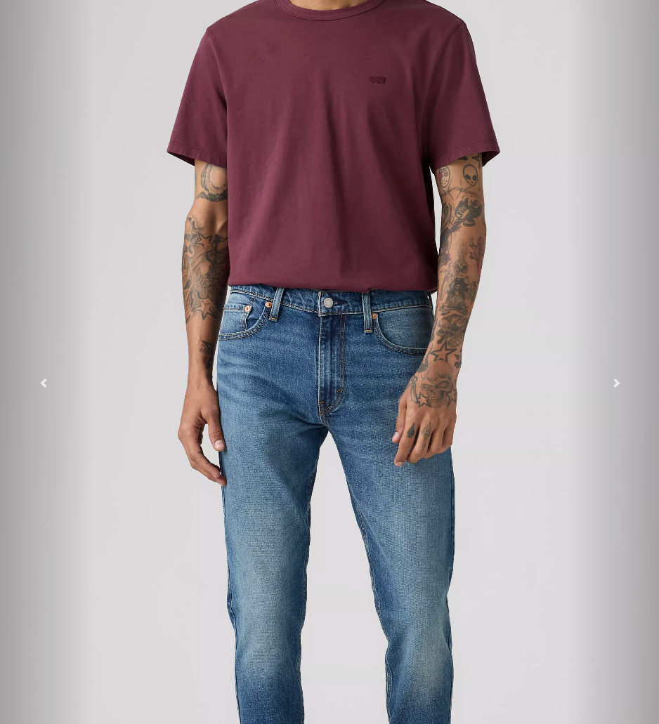 Man wearing a maroon t-shirt and blue jeans on a gray background