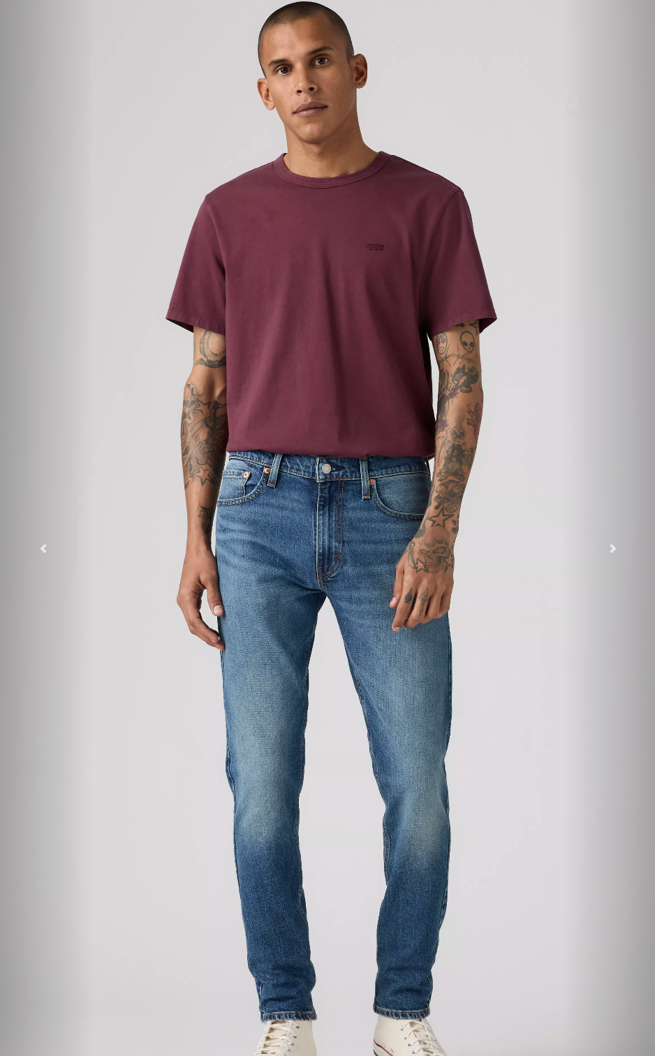 Man wearing a maroon t-shirt and blue jeans on a gray background