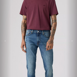 Man wearing a maroon t-shirt and blue jeans on a gray background