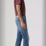 Person wearing a maroon t-shirt and blue jeans standing against a plain background