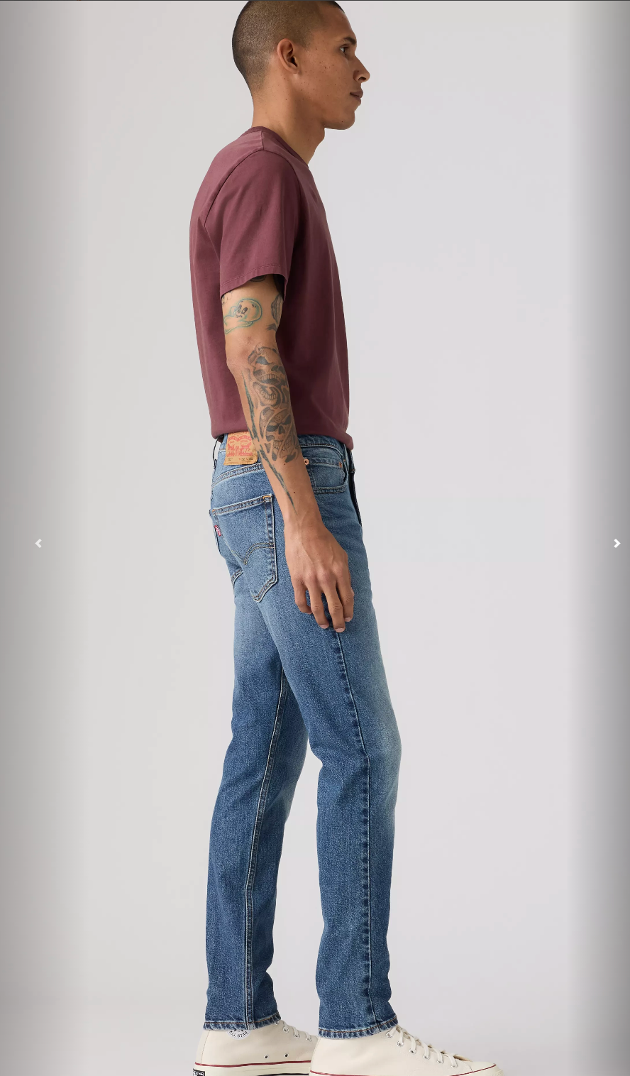 Person wearing a maroon t-shirt and blue jeans standing against a plain background