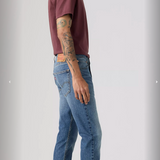 Person wearing a maroon t-shirt and blue jeans standing against a plain background