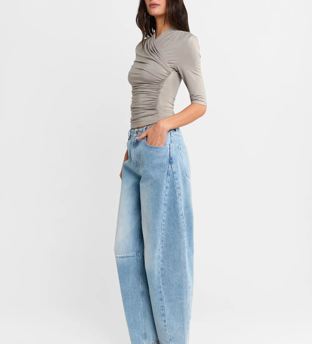 A woman shown from the side wearing a Steel grey half-sleeve ribbed  top and light-wash wide-leg denim jeans, paired with white heels, against a plain white studio background.