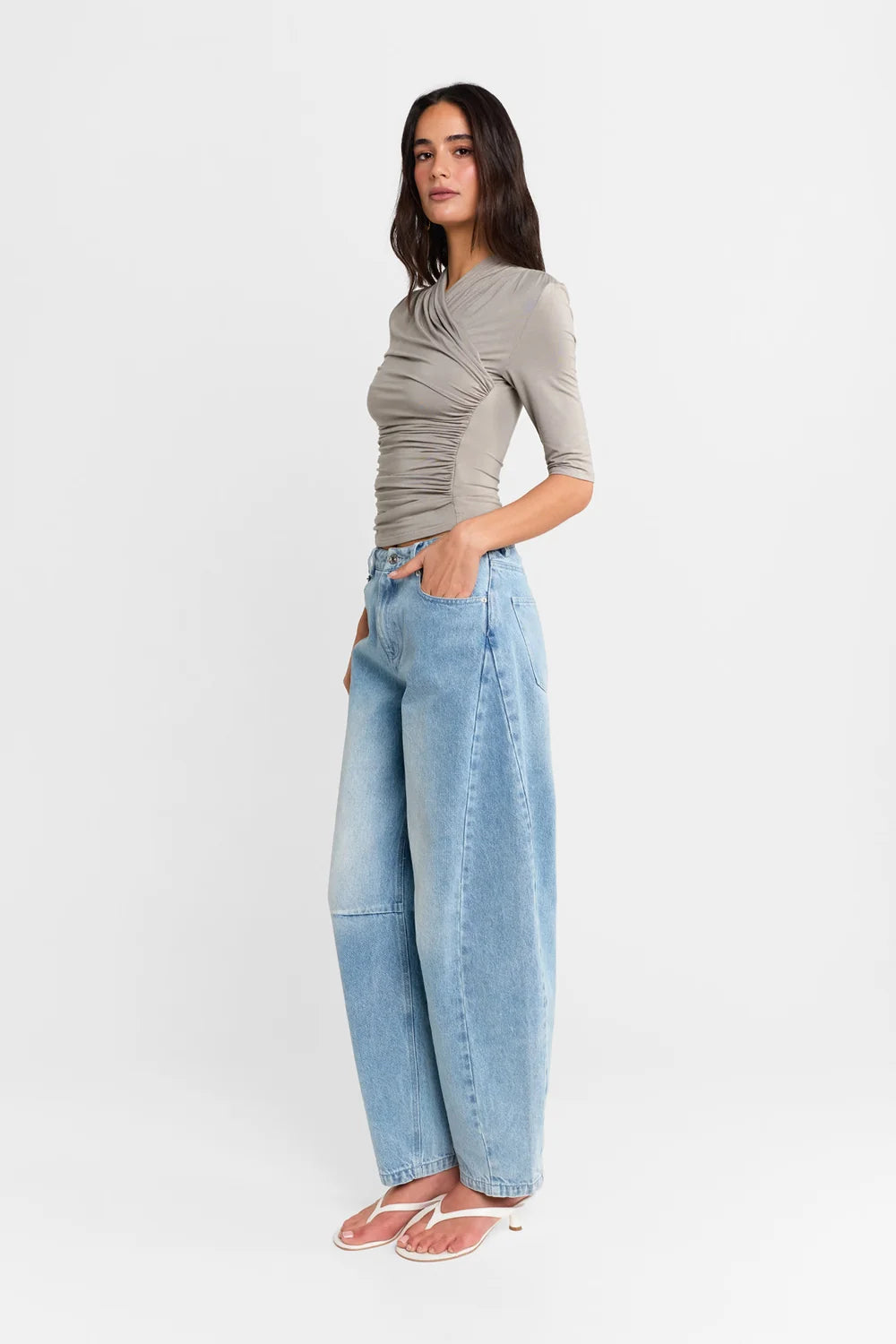 A woman shown from the side wearing a Steel grey half-sleeve ribbed  top and light-wash wide-leg denim jeans, paired with white heels, against a plain white studio background.
