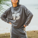 Person wearing a gray sweatshirt with a number 75 and pants outdoors.