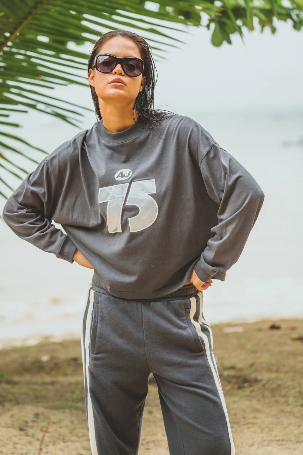 Person wearing a gray sweatshirt with a number 75 and pants outdoors.