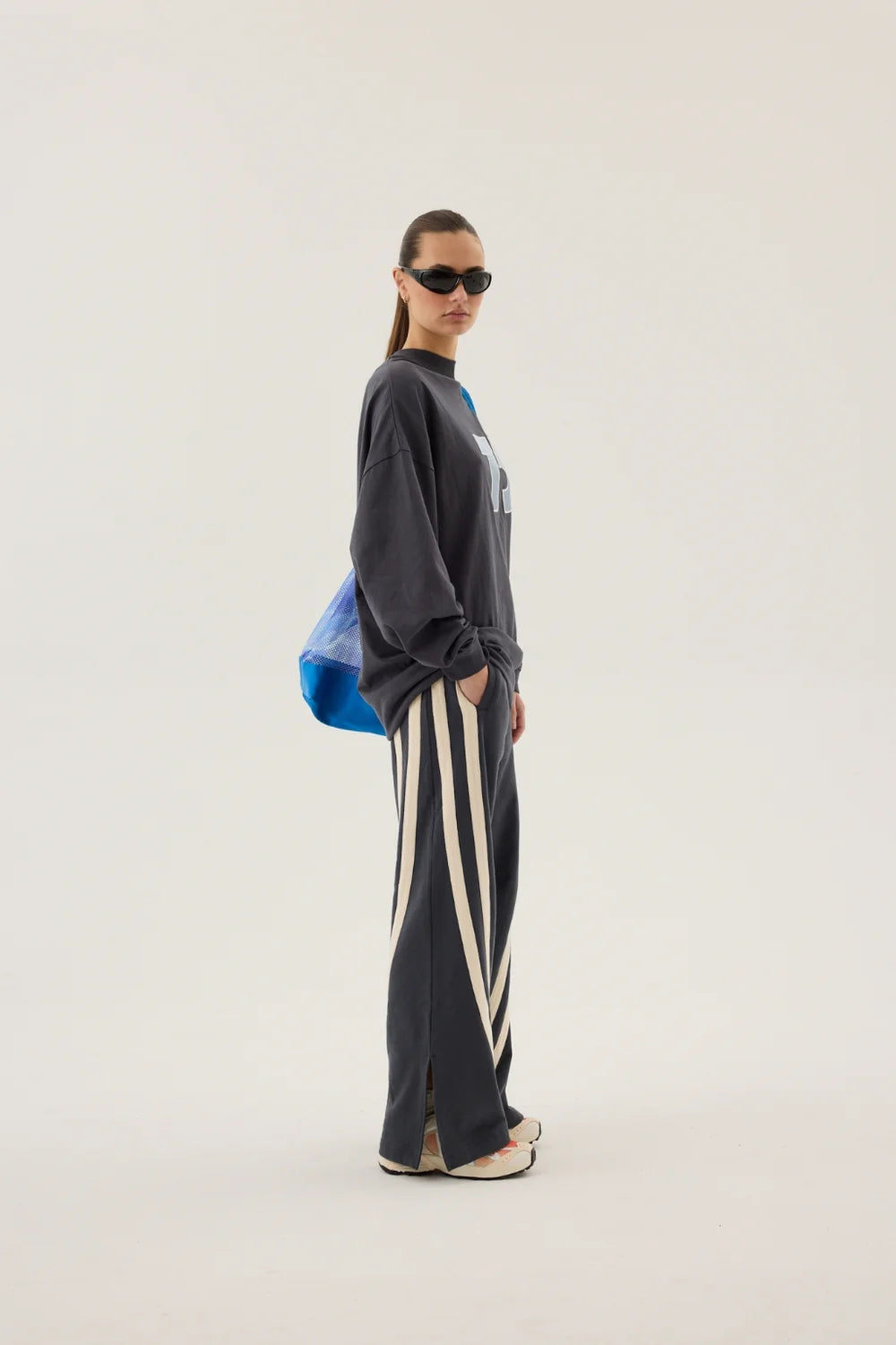 Person wearing a dark gray oversized sweatshirt and striped pants on a white background