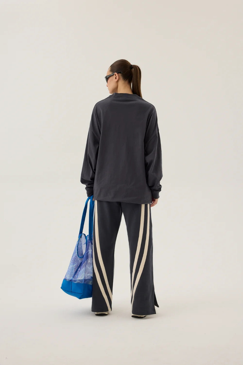 Person wearing a dark gray sweatshirt and pants with a blue bag on a white background