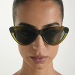 Person wearing a pair of green sunglasses with a neutral background