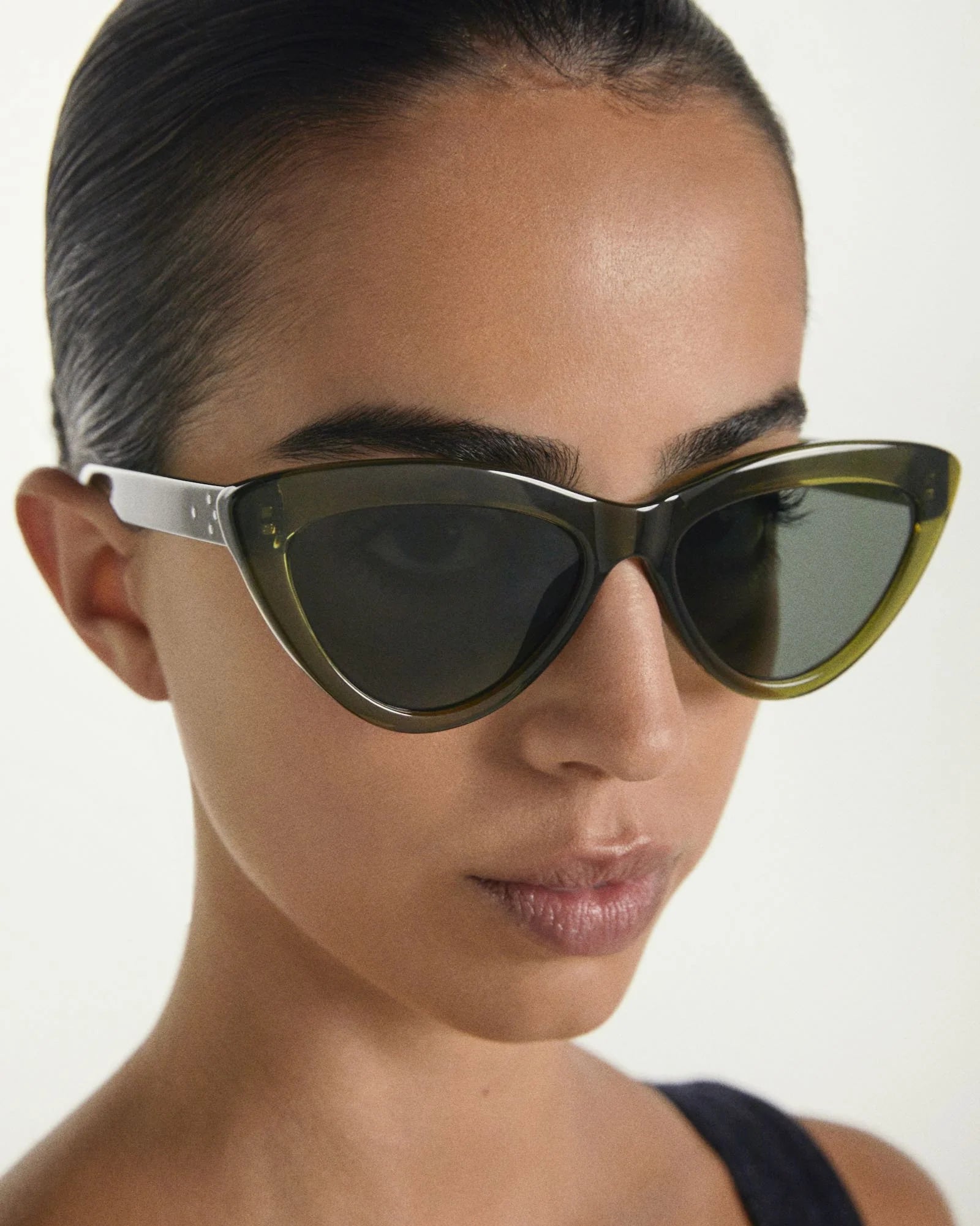 Person wearing a pair of cat-eye sunglasses with a neutral background