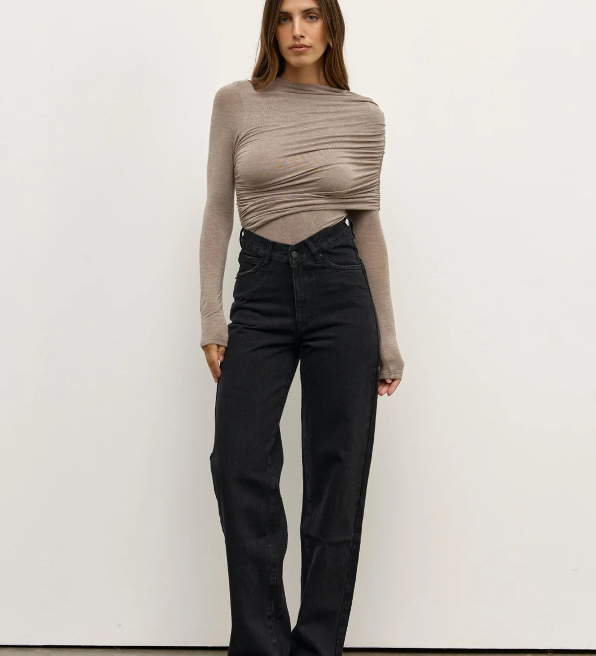 Woman wearing a beige long-sleeve top and black pants against a white background