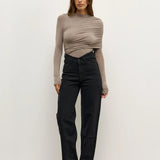 Woman wearing a beige long-sleeve top and black pants against a white background