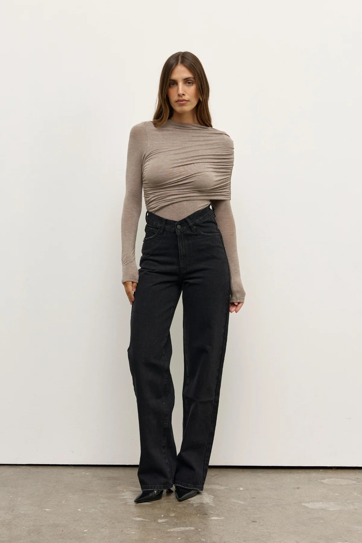 Woman wearing a beige long-sleeve top and black pants against a white background