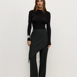 Woman wearing a black outfit with a skirt and long sleeves against a white background