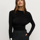 Woman wearing a black long-sleeve top and dark pants against a white background