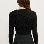 Woman wearing a black long-sleeve top and dark pants on a white background