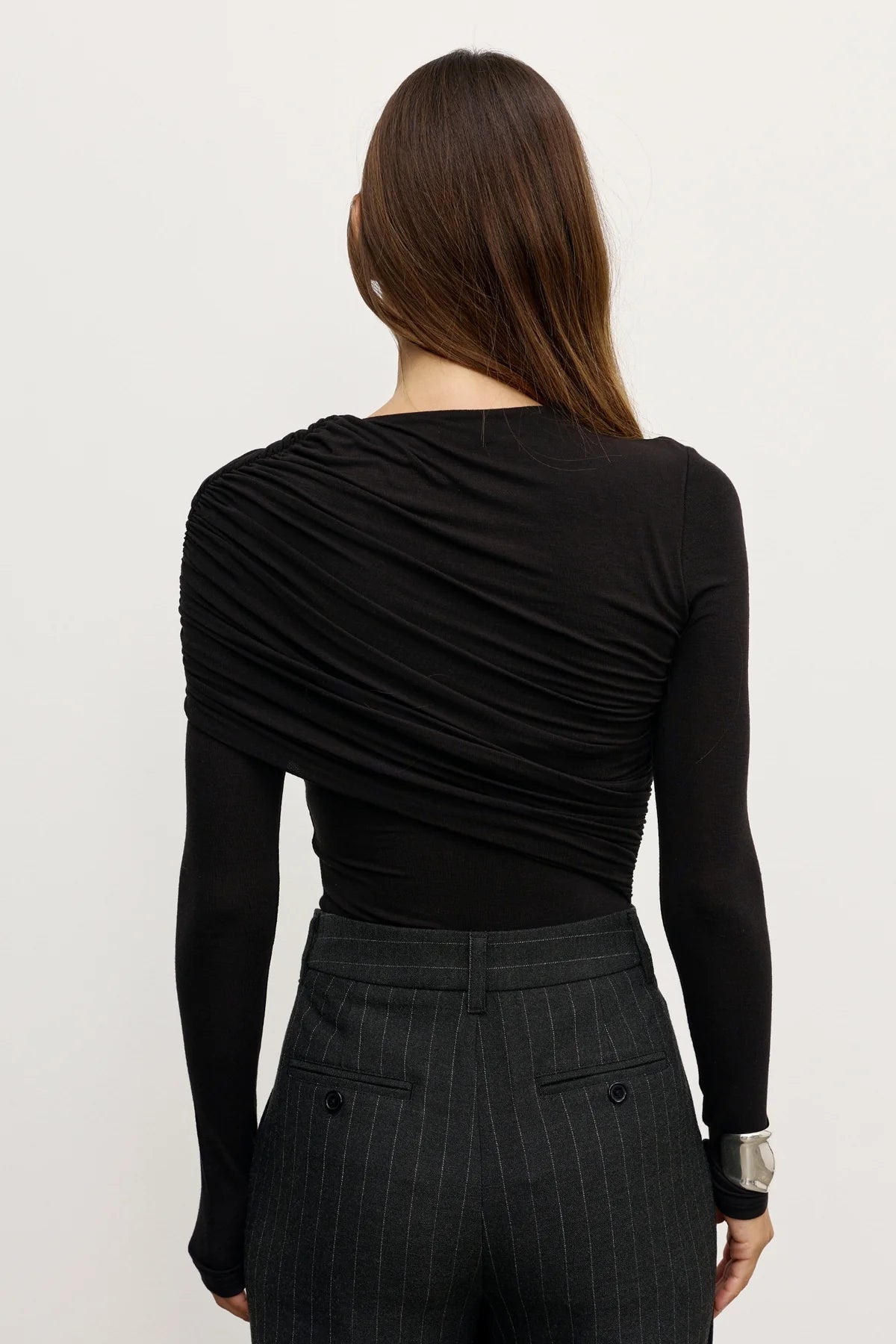 Woman wearing a black long-sleeve top and dark pants on a white background