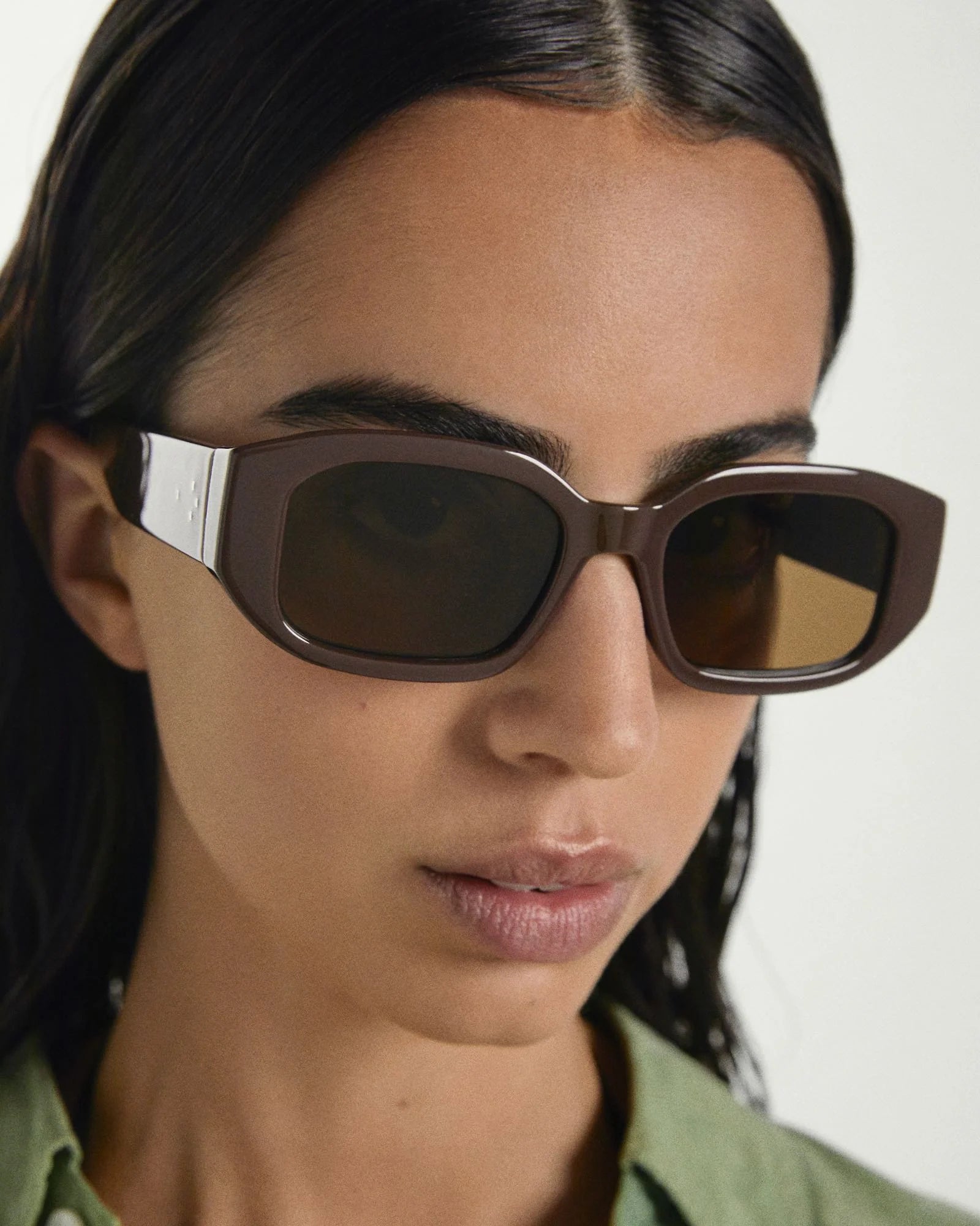 Person wearing a pair of sunglasses with a neutral background