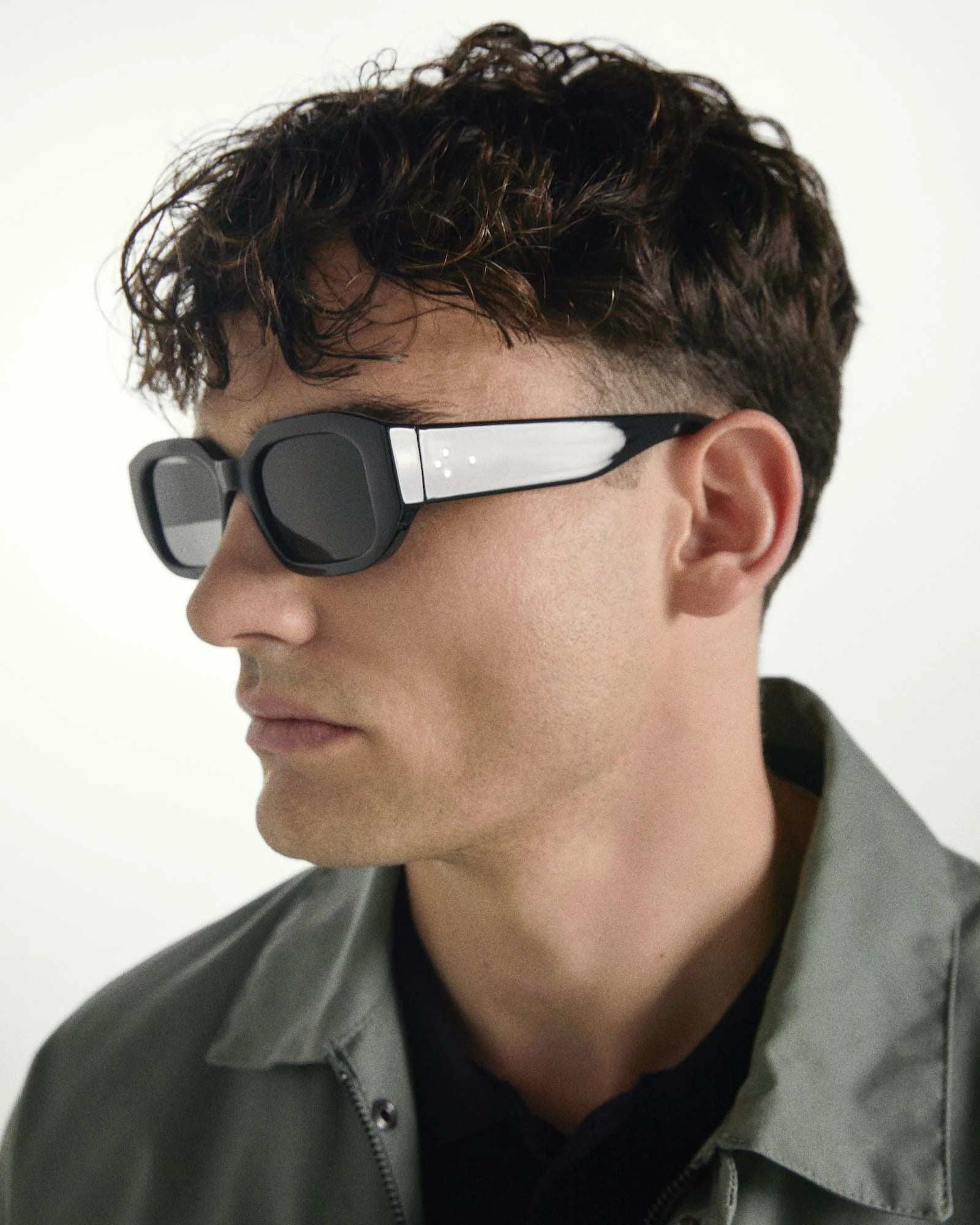 Person wearing black sunglasses with a white stripe on a plain background