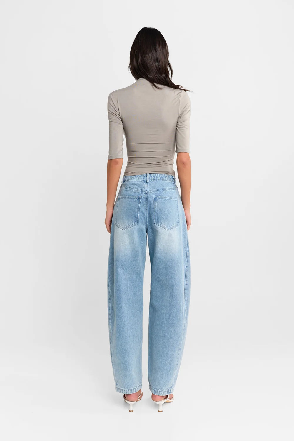 A woman shown from the back wearing a Steel grey half-sleeve ribbed  top and light-wash wide-leg denim jeans, paired with white heels, against a plain white studio background.