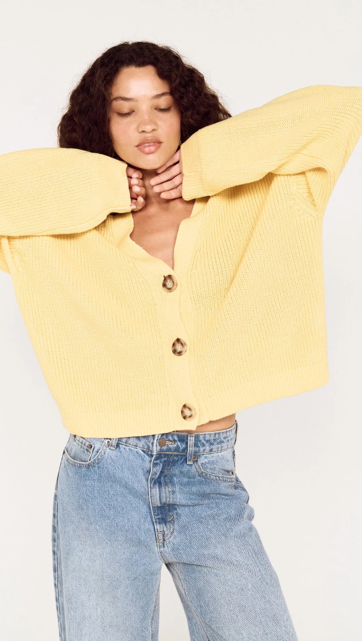 Person wearing a yellow sweater and light blue jeans on a white background