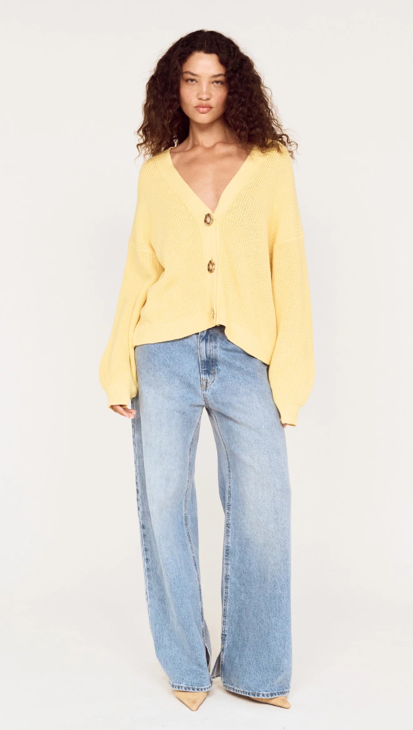 Person wearing a yellow sweater and light blue jeans on a white background