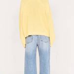 Person wearing a yellow sweater and light blue jeans on a white background