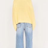 Person wearing a yellow sweater and light blue jeans on a white background