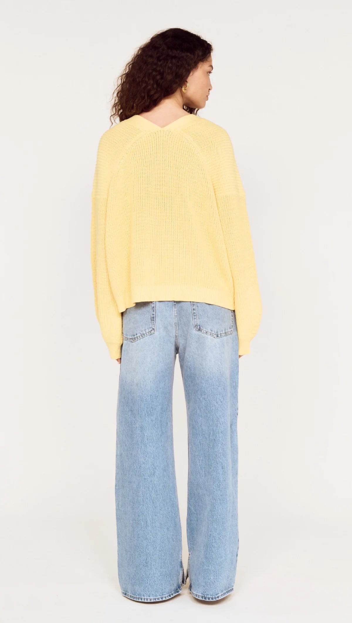 Person wearing a yellow sweater and light blue jeans on a white background