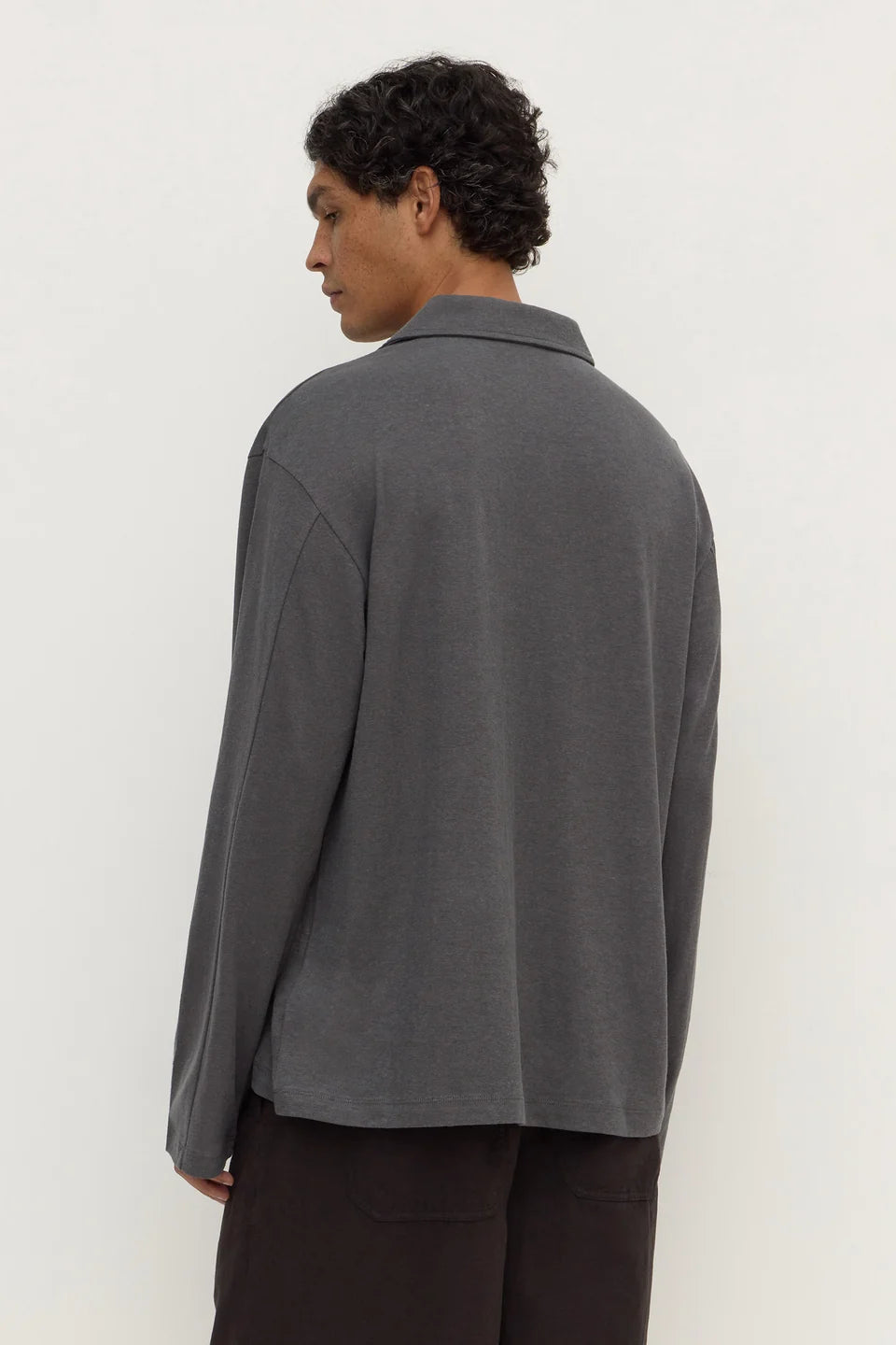 A man wearing a dark gray long-sleeve knit polo shirt, shown from the back against a plain off-white background.