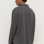 A man wearing a dark gray long-sleeve knit polo shirt, shown from the back against a plain off-white background.