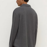 A man wearing a dark gray long-sleeve knit polo shirt, shown from the back against a plain off-white background.