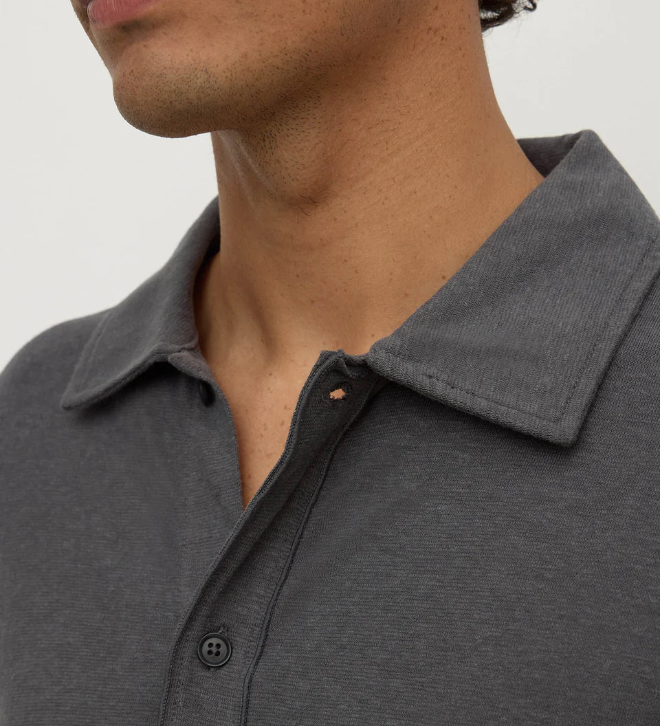 Close-up of a man wearing a dark gray heathered polo shirt, showing the collar, button placket, and part of his neck and lower face against a plain light background.