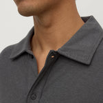Close-up of a man wearing a dark gray heathered polo shirt, showing the collar, button placket, and part of his neck and lower face against a plain light background.