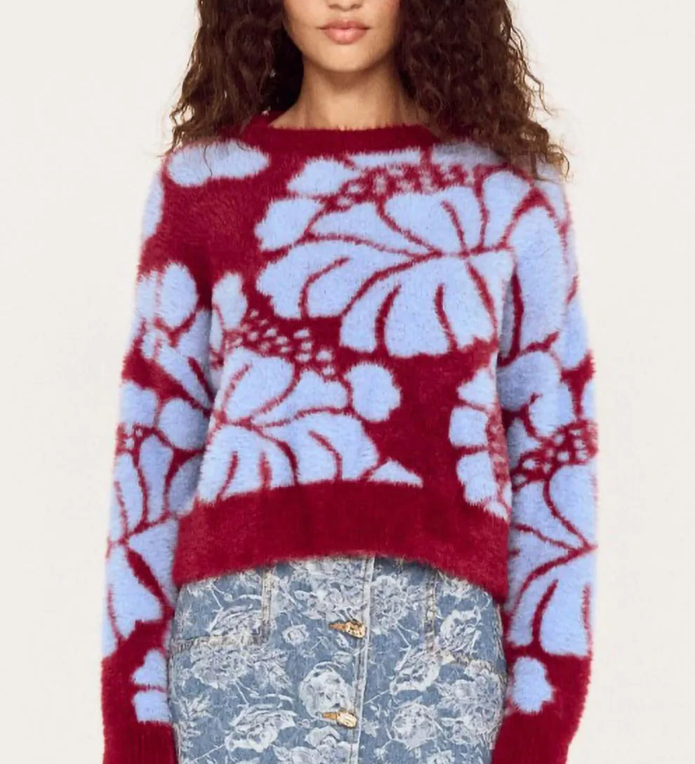 Woman wearing a red and blue floral-patterned sweater with a denim skirt on a white background