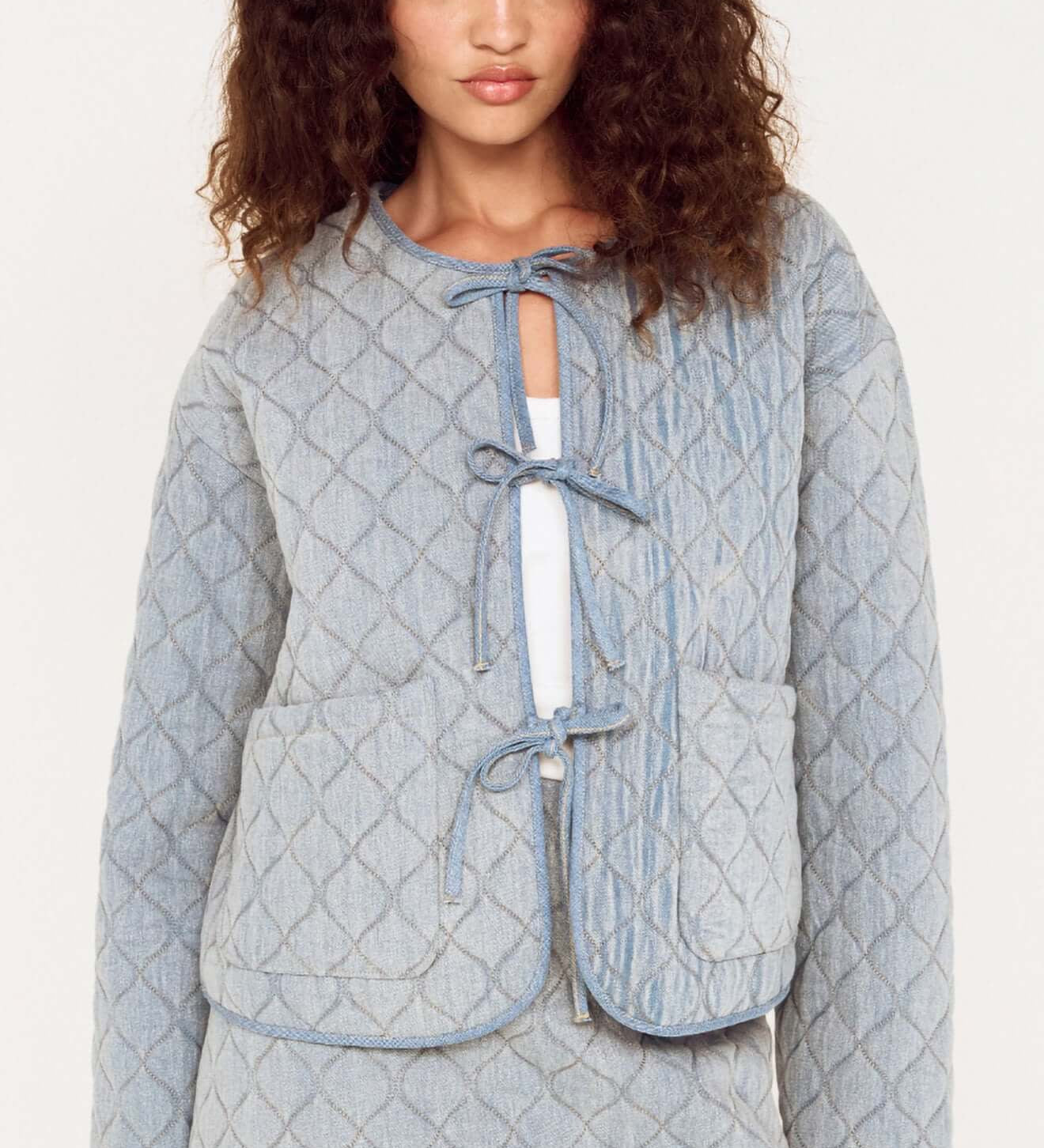 Woman wearing a light blue quilted jacket and skirt set on a white background