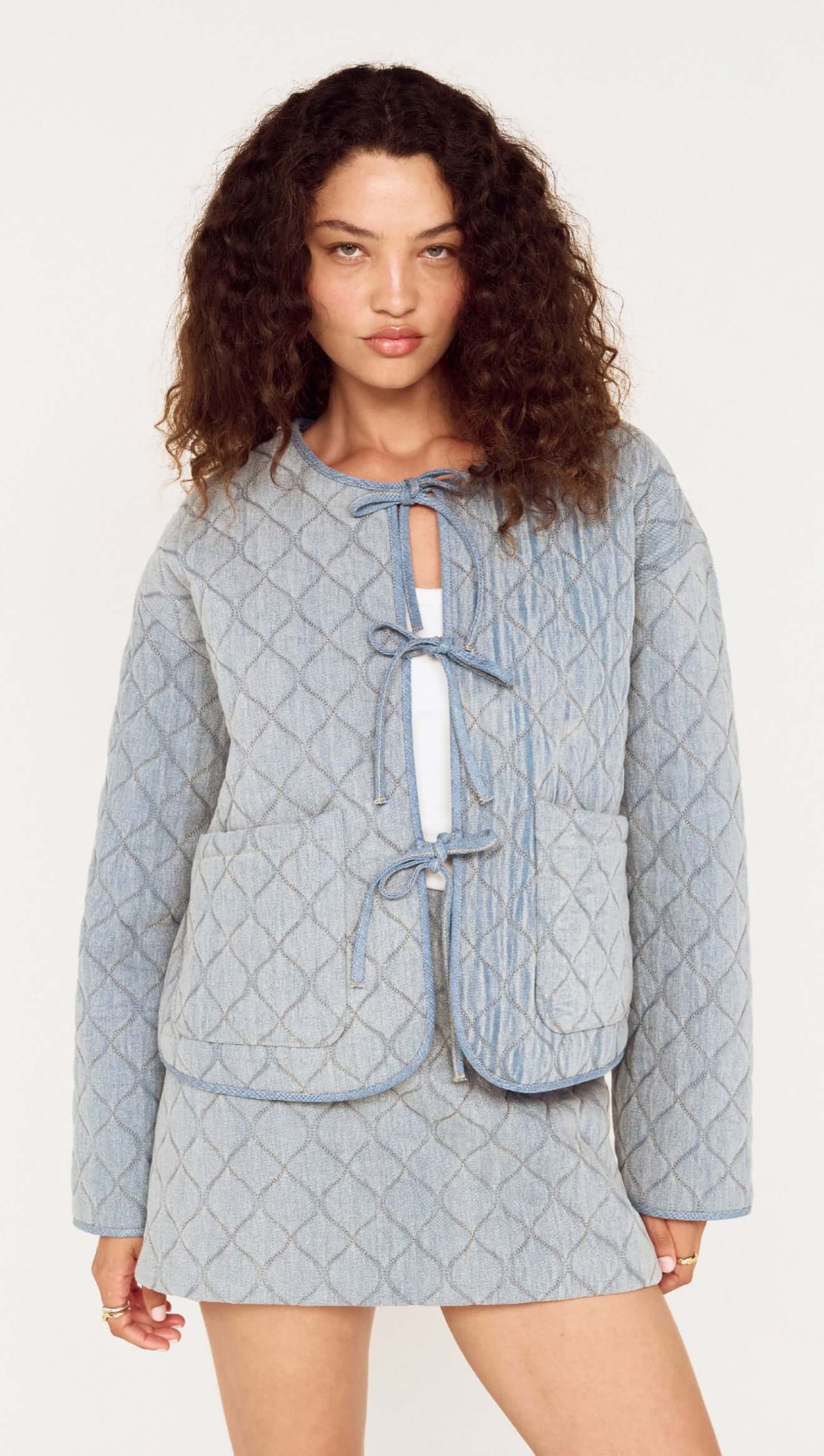 Woman wearing a light blue quilted jacket and skirt set on a white background