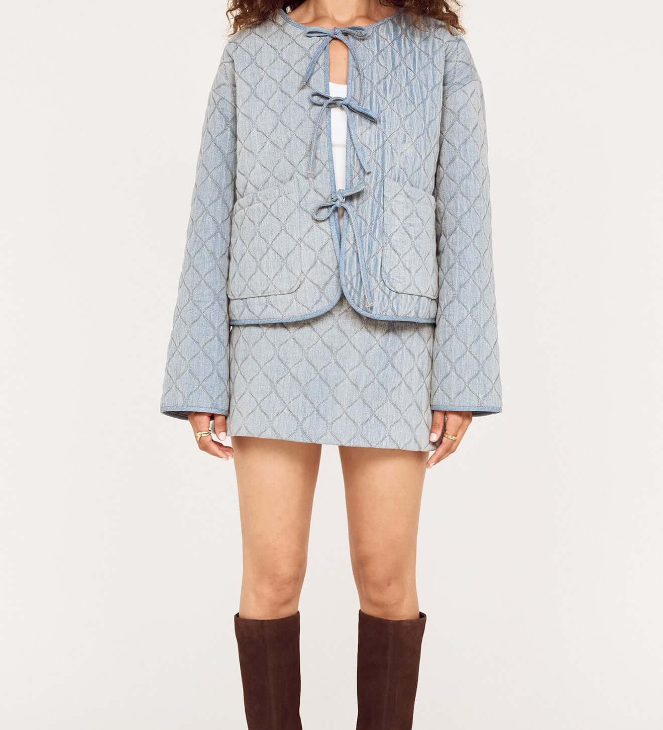 Woman wearing a light blue textured jacket and skirt set with brown knee-high boots on a white background