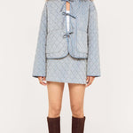 Woman wearing a light blue textured jacket and skirt set with brown knee-high boots on a white background