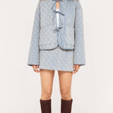 Woman wearing a light blue textured jacket and skirt set with brown knee-high boots on a white background