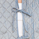 Light blue quilted jacket with tied front design over a white top.