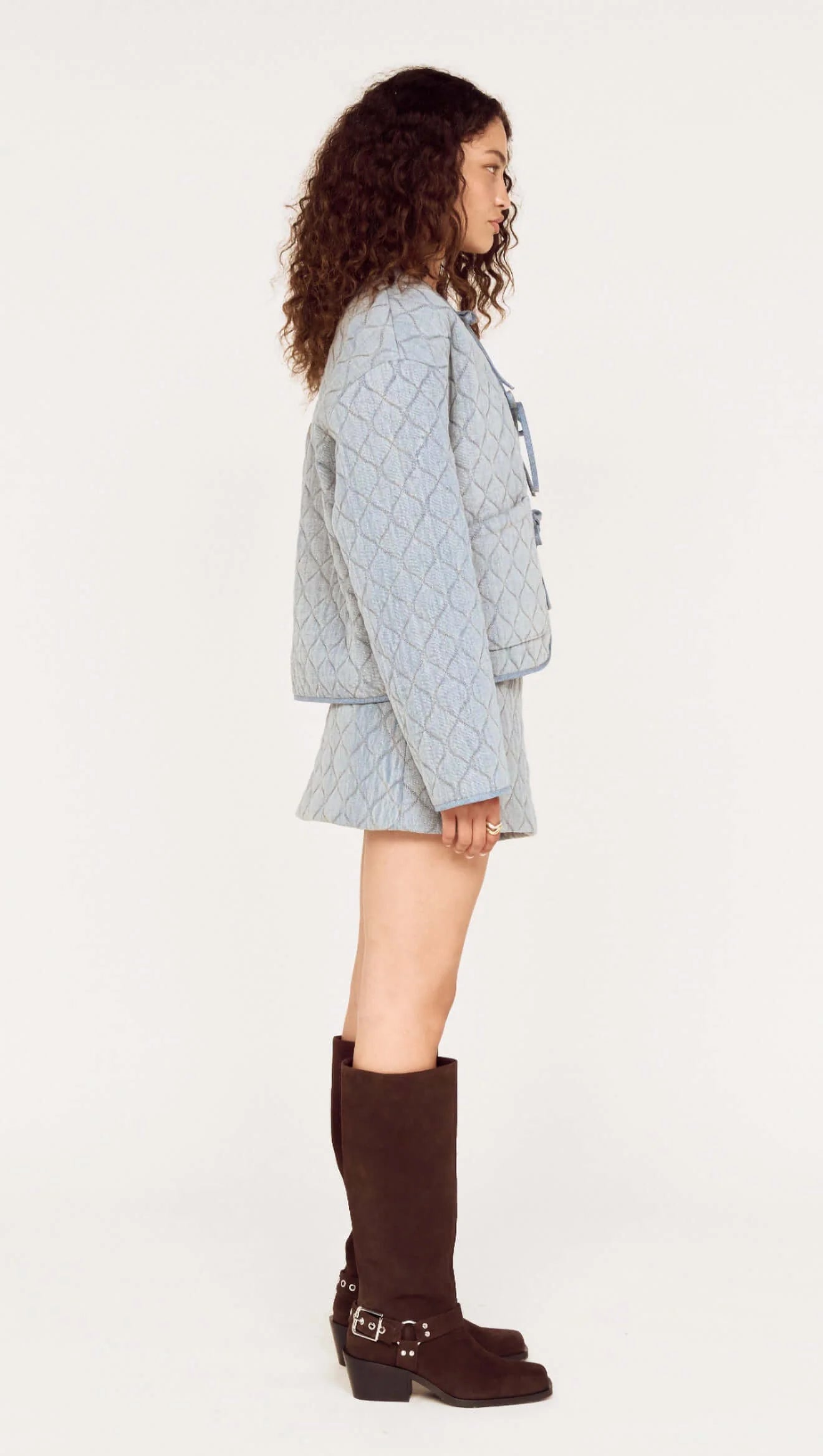 Woman wearing a light blue quilted jacket and brown knee-high boots on a white background