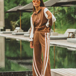 Woman in a brown tracksuit with white stripes standing by a poolside.
