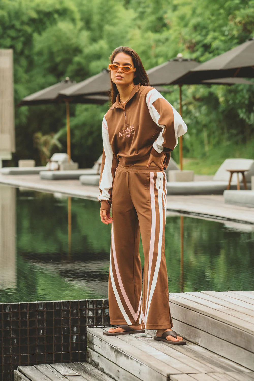 Woman in a brown tracksuit with white stripes standing by a poolside.