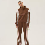 Person wearing a brown tracksuit with white stripes and 'AJames' branding on a beige background