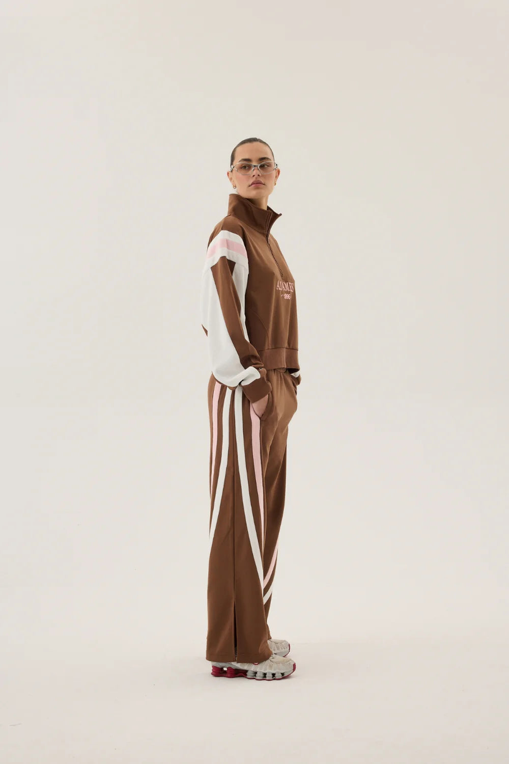 Person wearing a brown tracksuit with white stripes on a plain background