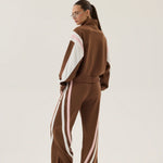 Person wearing a brown tracksuit with white stripes on a plain background
